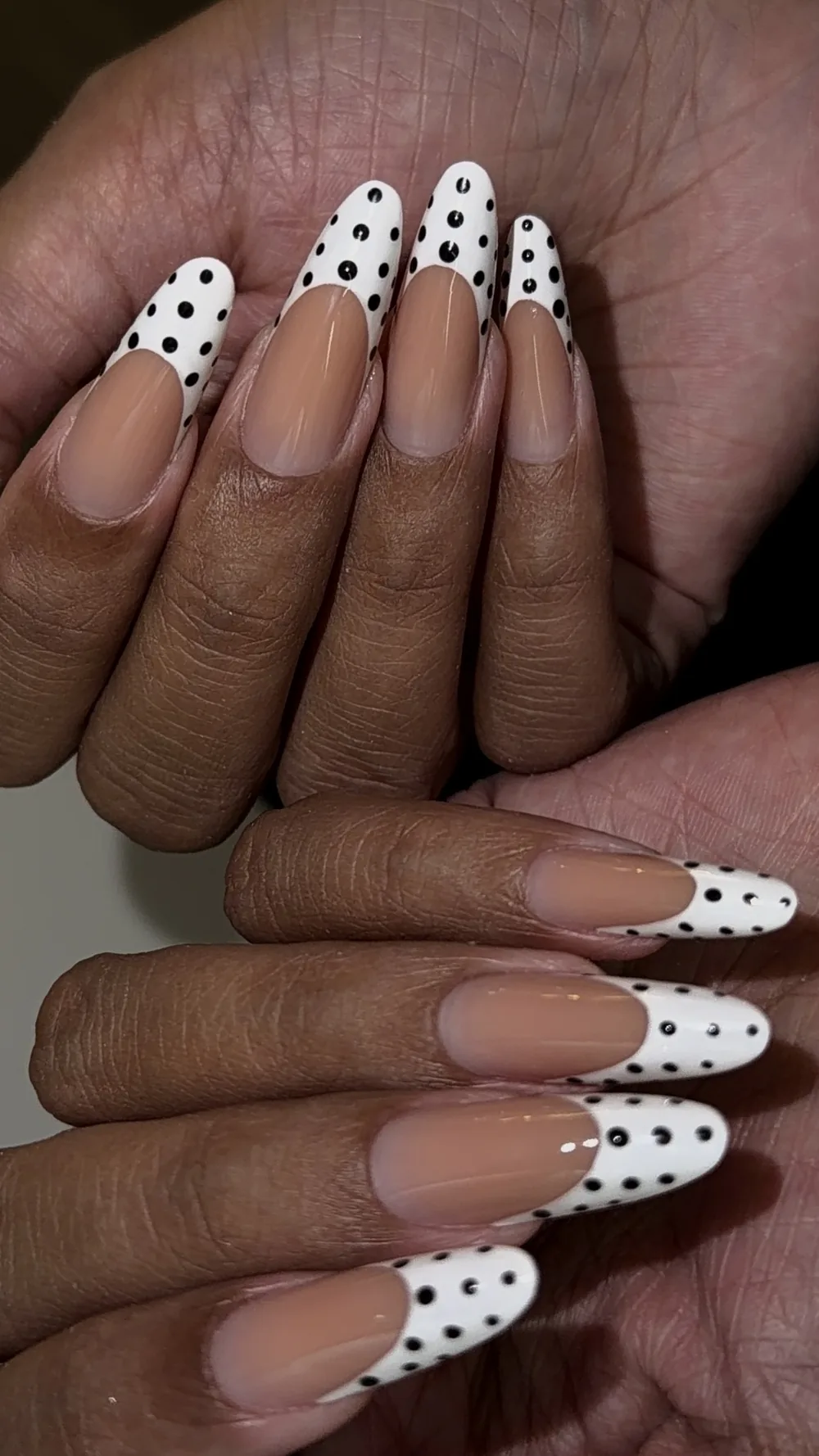White French tips with hand-painted black polka dots on almond nails